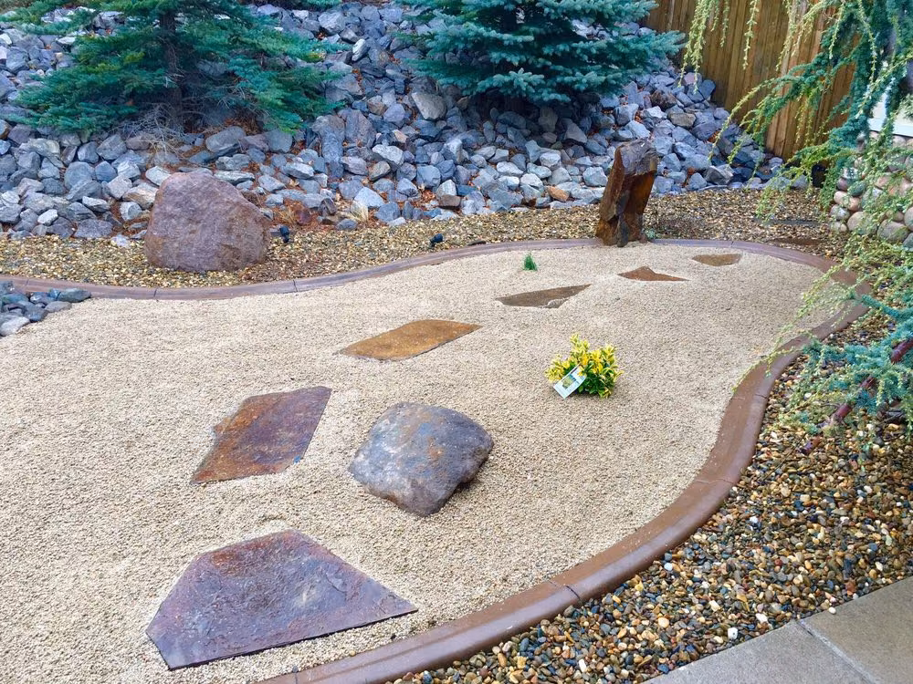 Cut flagstone stepping pads and boulders set in tan gravel, with a vertical stone accent